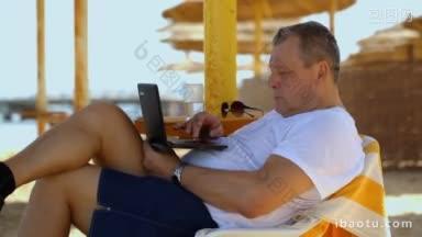 男子放松与笔记本电脑在海滩度假村斜靠在舒适的椅子下的稻草沙滩伞凝视